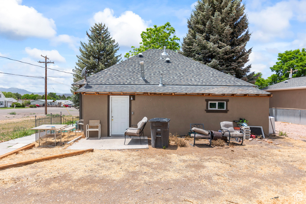Rear view of house featuring a shingled roof, stucco siding, a patio, and a mountain view