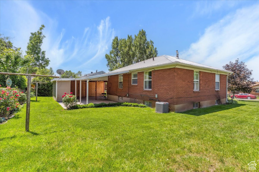 Rear view of property with central AC unit, a patio area, a lawn, brick siding, and metal roof