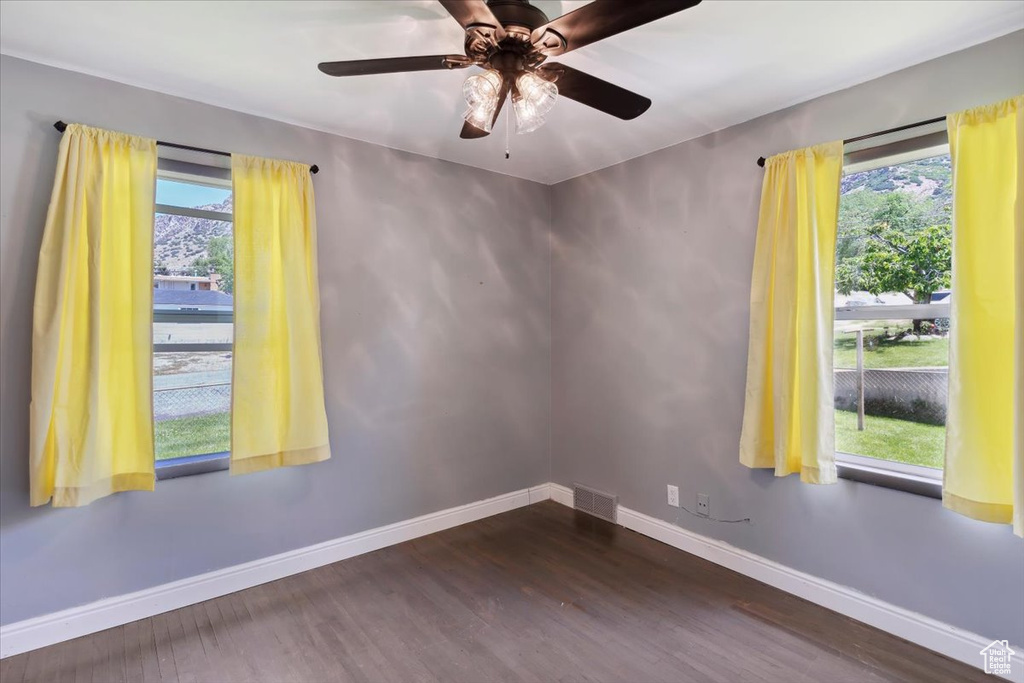 Unfurnished room featuring plenty of natural light, baseboards, dark wood-style floors, and a ceiling fan