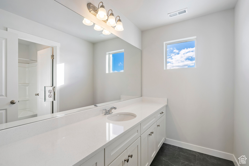 Full bath featuring vanity, baseboards, marble look tiles, and a shower