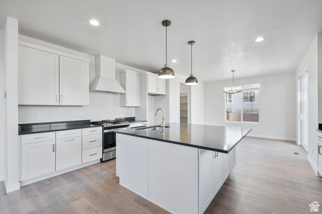 Kitchen with gas stove, custom range hood, a sink, dark countertops, and light wood-style flooring