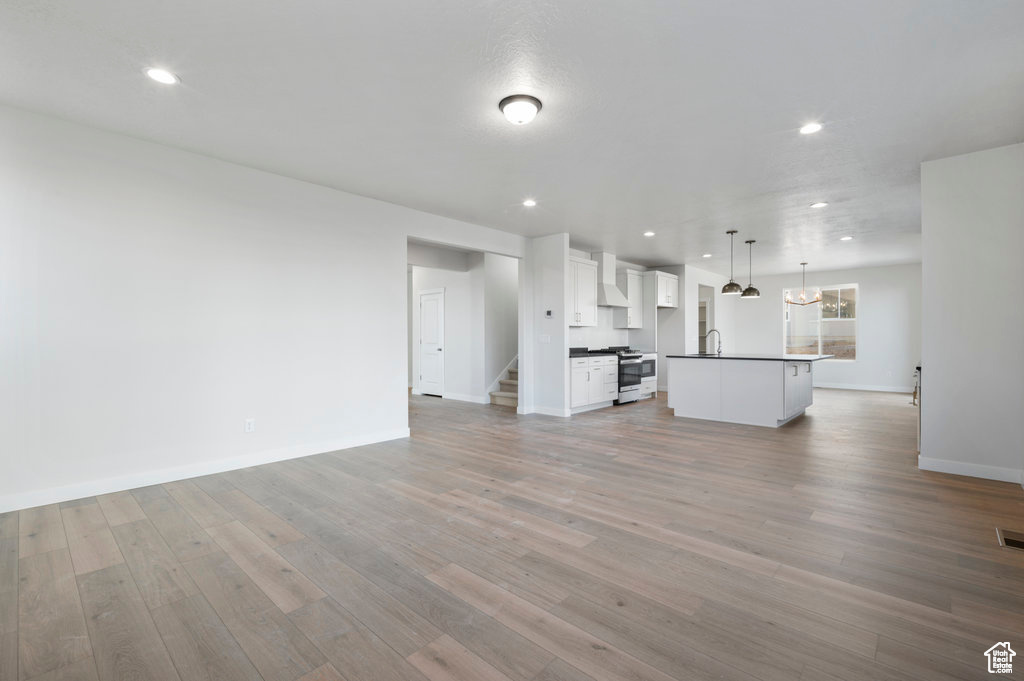 Unfurnished living room featuring recessed lighting, light wood-style flooring, baseboards, a sink, and stairway