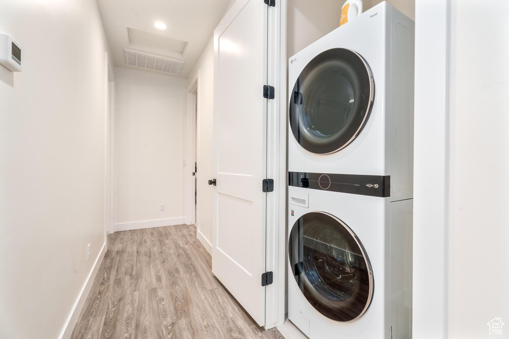 Washroom featuring stacked washing machine and dryer, light wood-type flooring, baseboards, attic access, and recessed lighting
