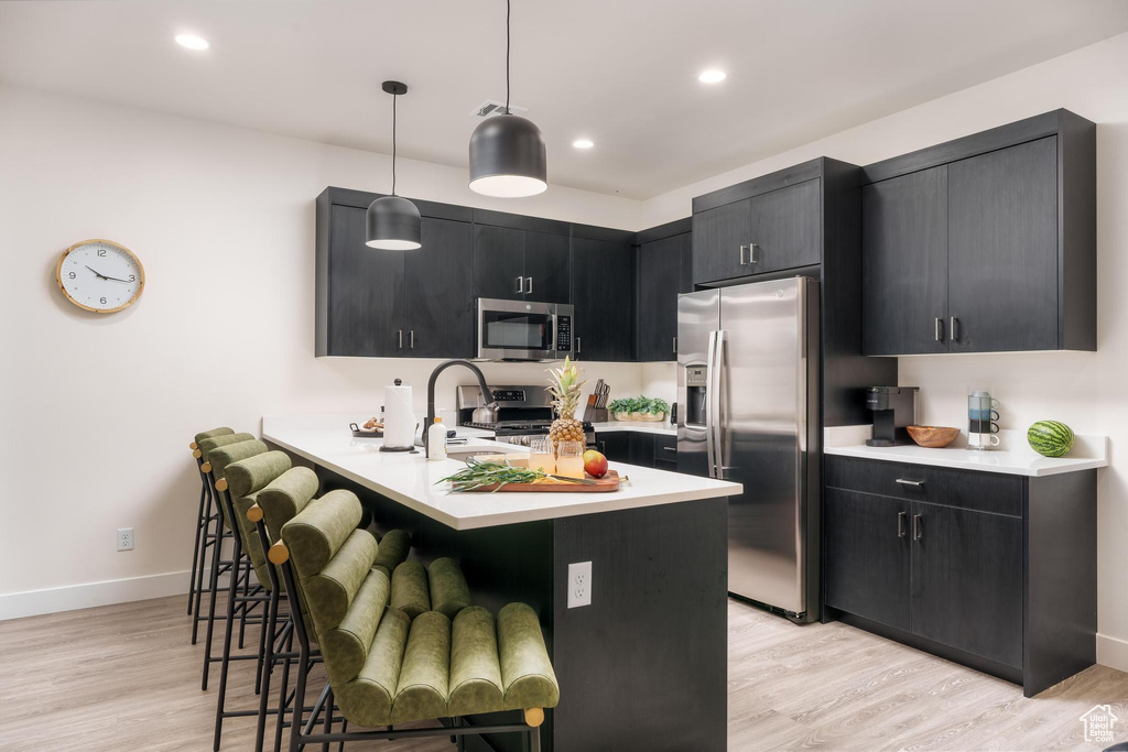 Kitchen featuring stainless steel appliances, dark cabinets, light countertops, a breakfast bar, and recessed lighting