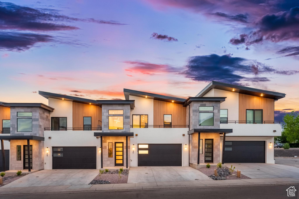 Modern home with a balcony, a garage, driveway, and stone siding