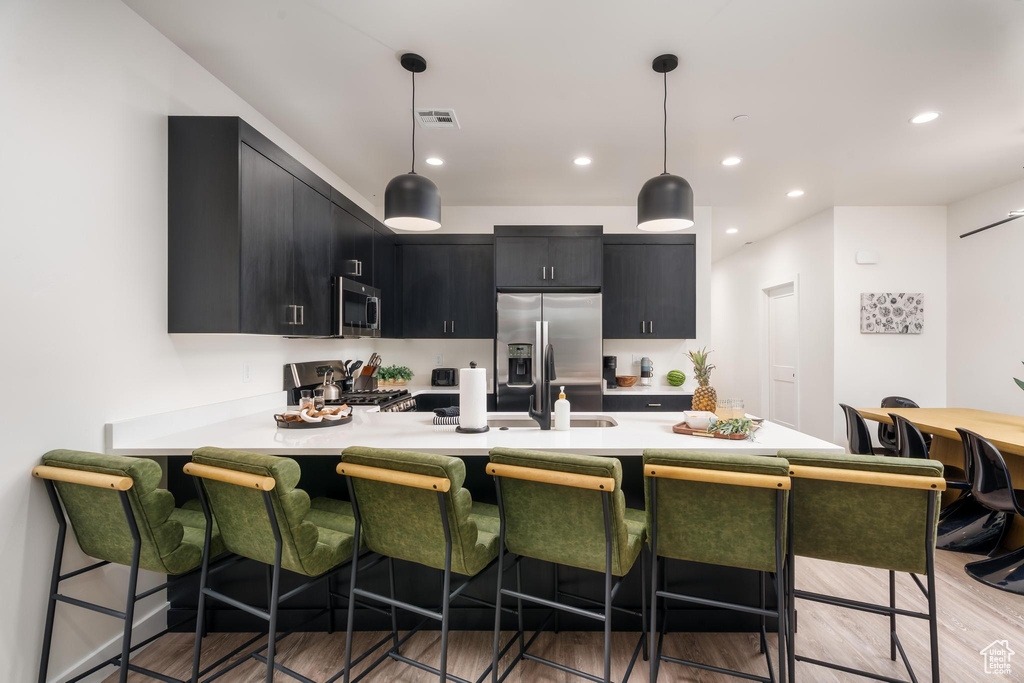 Kitchen featuring dark cabinets, stainless steel appliances, light countertops, a peninsula, and a breakfast bar