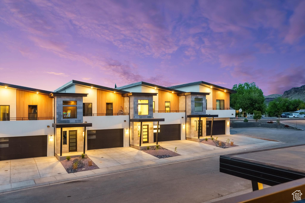 Modern home featuring a balcony, an attached garage, concrete driveway, and stucco siding