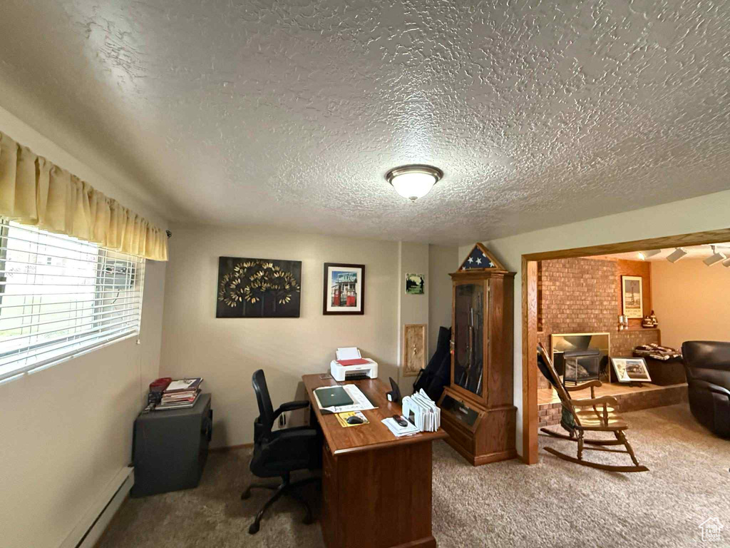Office area featuring a textured ceiling, carpet flooring, a baseboard heating unit, and baseboards