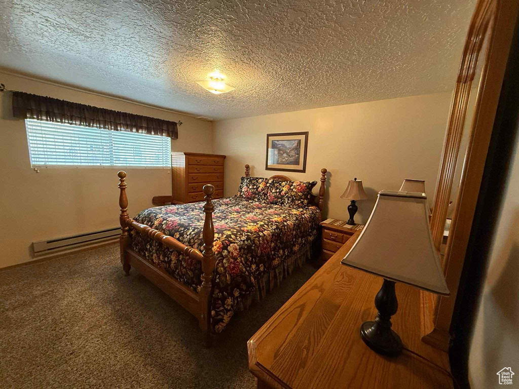 Carpeted bedroom with a baseboard heating unit and a textured ceiling