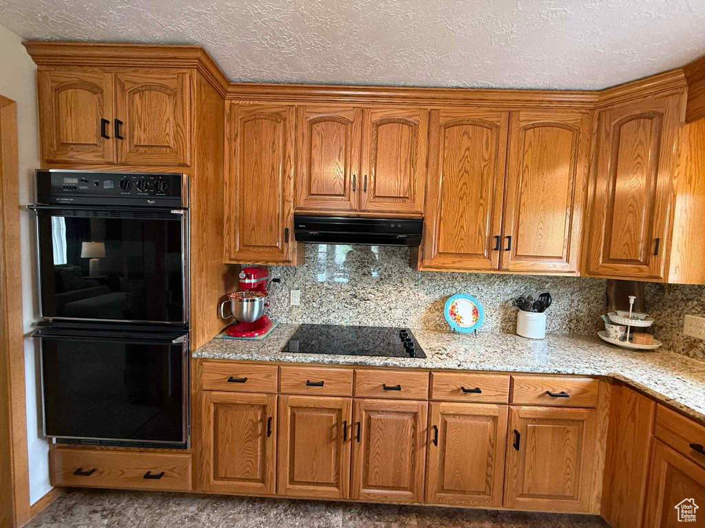 Kitchen featuring black appliances, ventilation hood, brown cabinets, and a textured ceiling