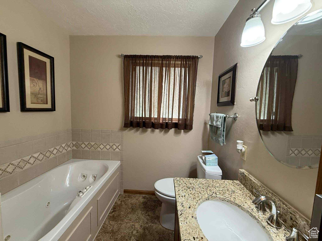 Bathroom featuring toilet, a jetted tub, vanity, and a textured ceiling