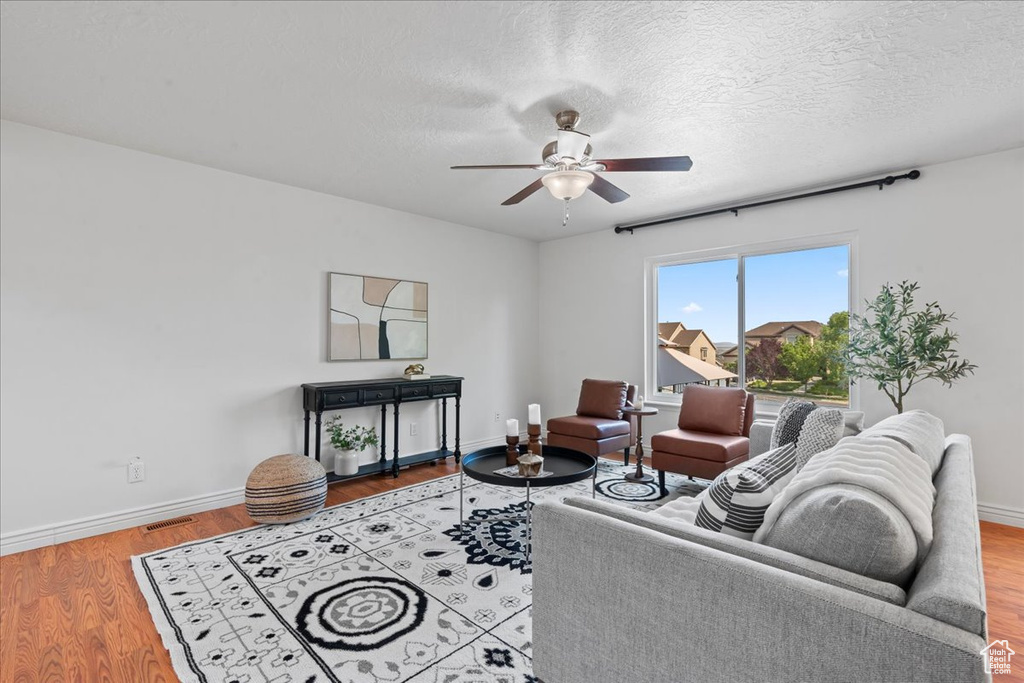 Living area featuring ceiling fan, baseboards, wood finished floors, and a textured ceiling
