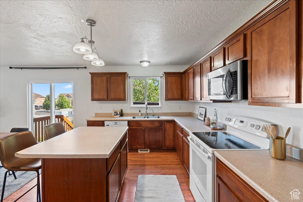 Kitchen featuring white appliances, a sink, a textured ceiling, light countertops, and dark wood finished floors