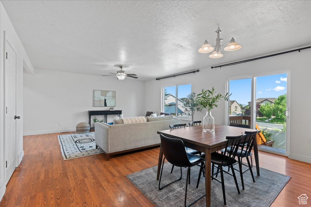 Dining room featuring ceiling fan, a textured ceiling, wood finished floors, a chandelier, and baseboards