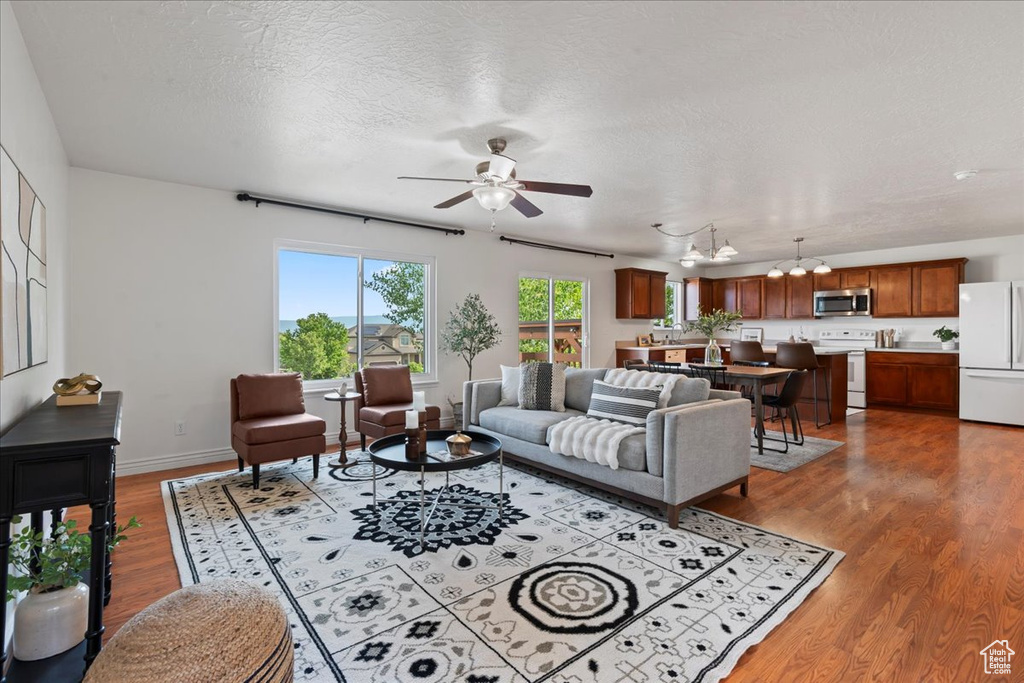 Living area featuring wood finished floors, a ceiling fan, a textured ceiling, a chandelier, and baseboards