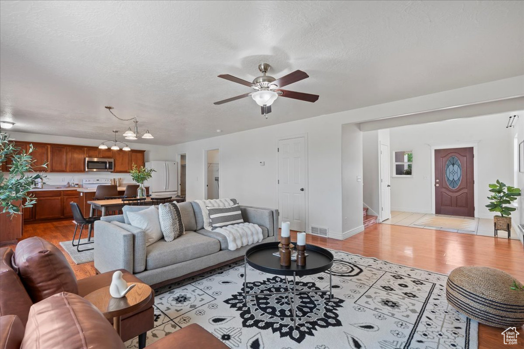 Living area with a chandelier, a ceiling fan, stairway, light wood-style floors, and baseboards
