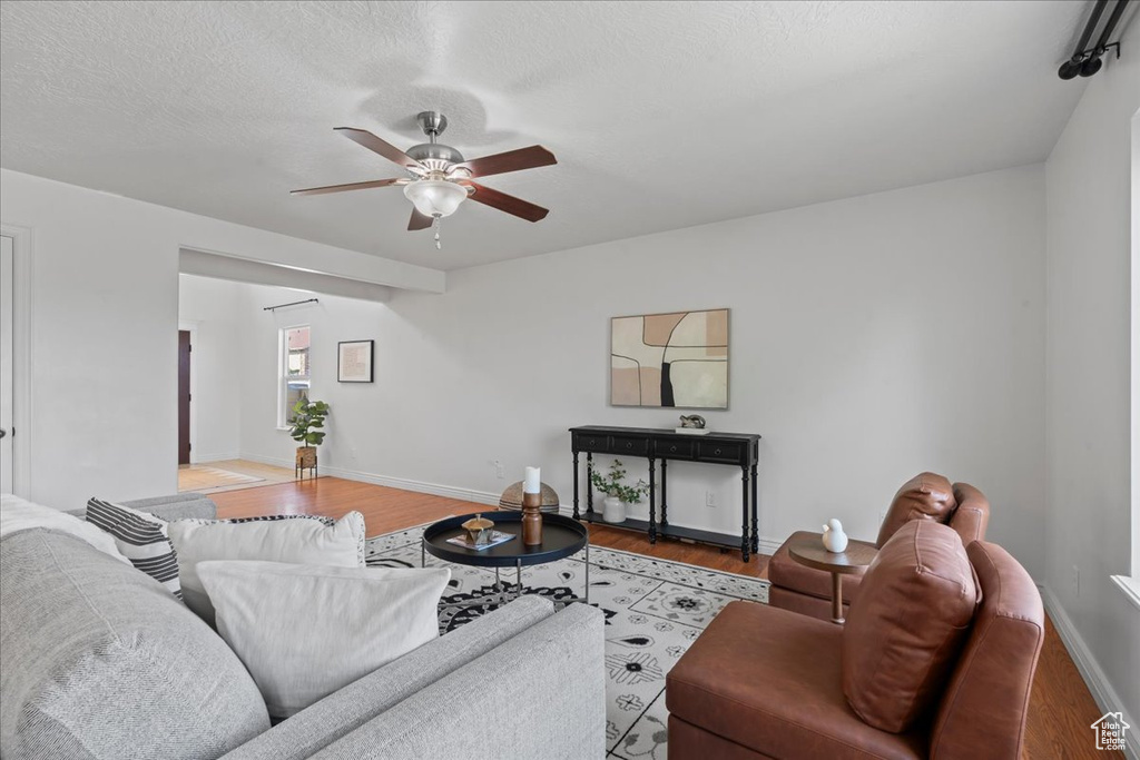 Living area with a ceiling fan, wood finished floors, baseboards, and a textured ceiling