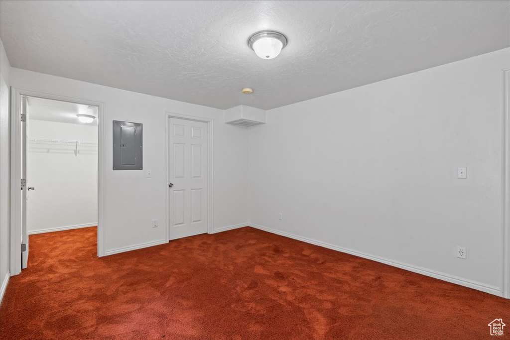 Unfurnished bedroom with electric panel, dark carpet, a walk in closet, baseboards, and a closet