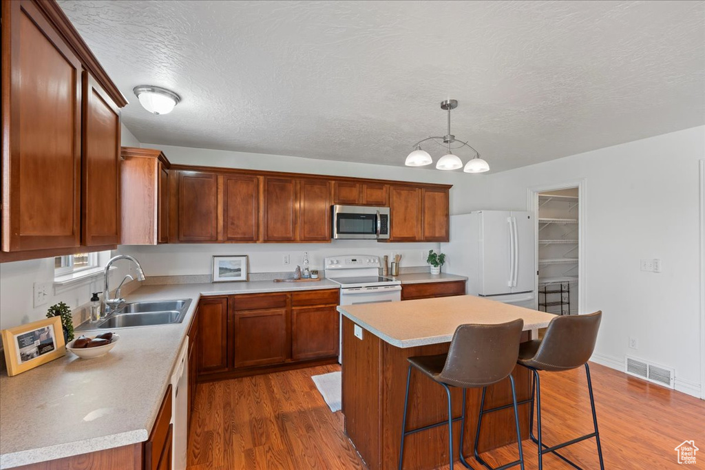 Kitchen with white appliances, a sink, dark wood-style flooring, a center island, and a textured ceiling