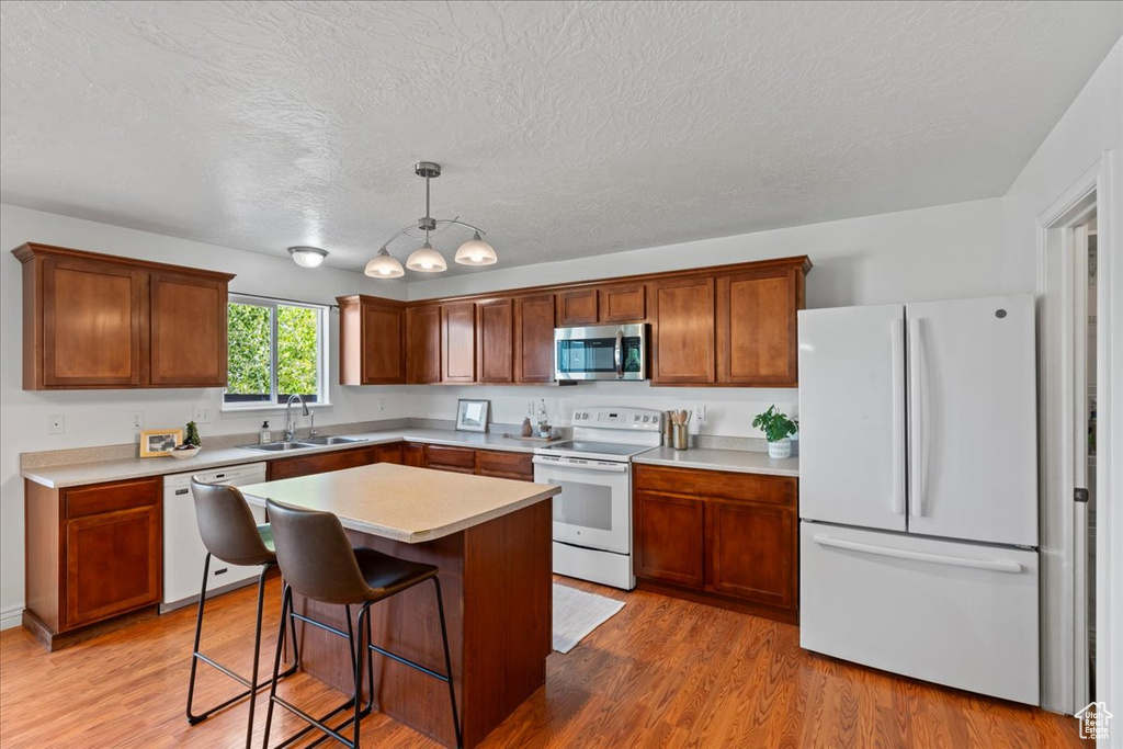 Kitchen with white appliances, a sink, light countertops, a textured ceiling, and light wood finished floors