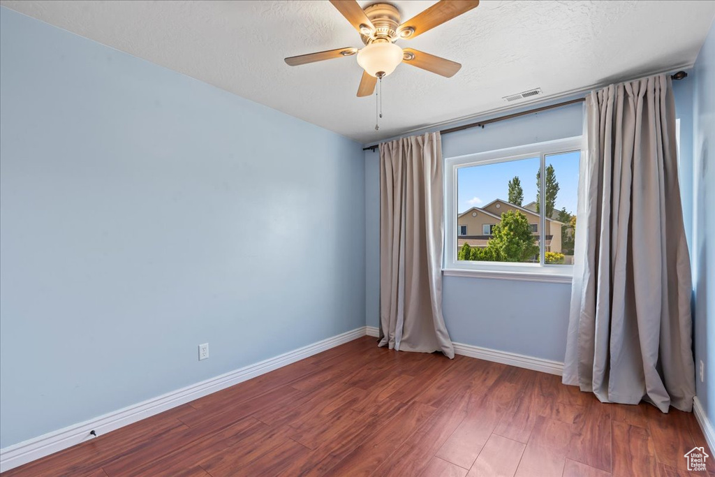 Empty room featuring baseboards, wood finished floors, a ceiling fan, and a textured ceiling