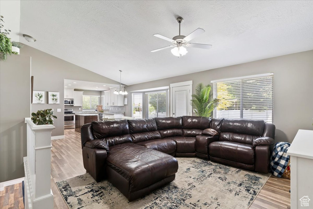 Living area featuring a textured ceiling, a ceiling fan, lofted ceiling, light wood-style floors, and a chandelier