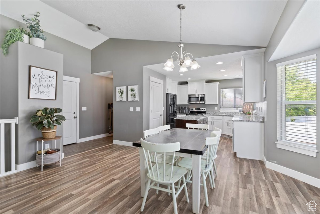 Dining space with wood finished floors, a chandelier, baseboards, and high vaulted ceiling