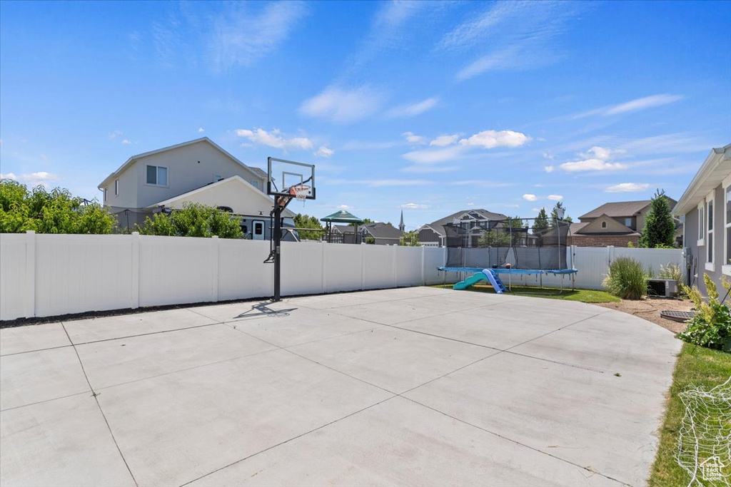 View of basketball court featuring a trampoline, a fenced backyard, a residential view, and basketball hoop