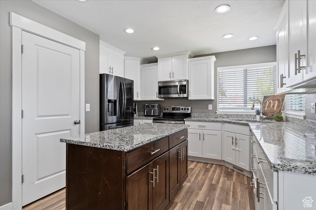 Kitchen featuring stainless steel appliances, light wood-style floors, white cabinets, dark brown cabinetry, and recessed lighting