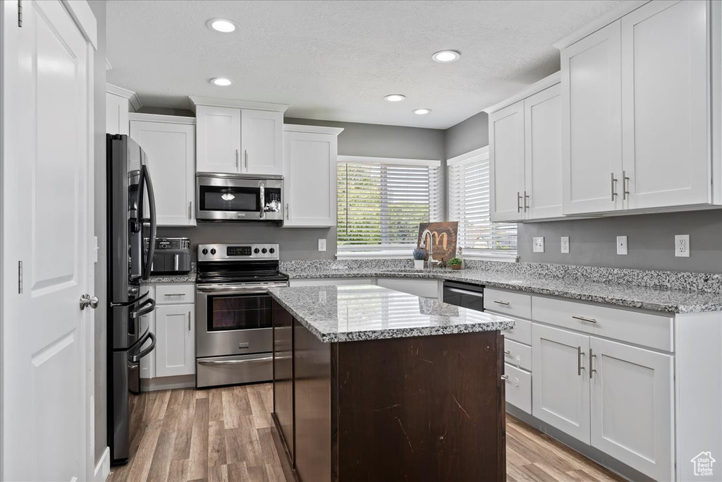 Kitchen with stainless steel appliances, light wood finished floors, white cabinetry, recessed lighting, and a textured ceiling