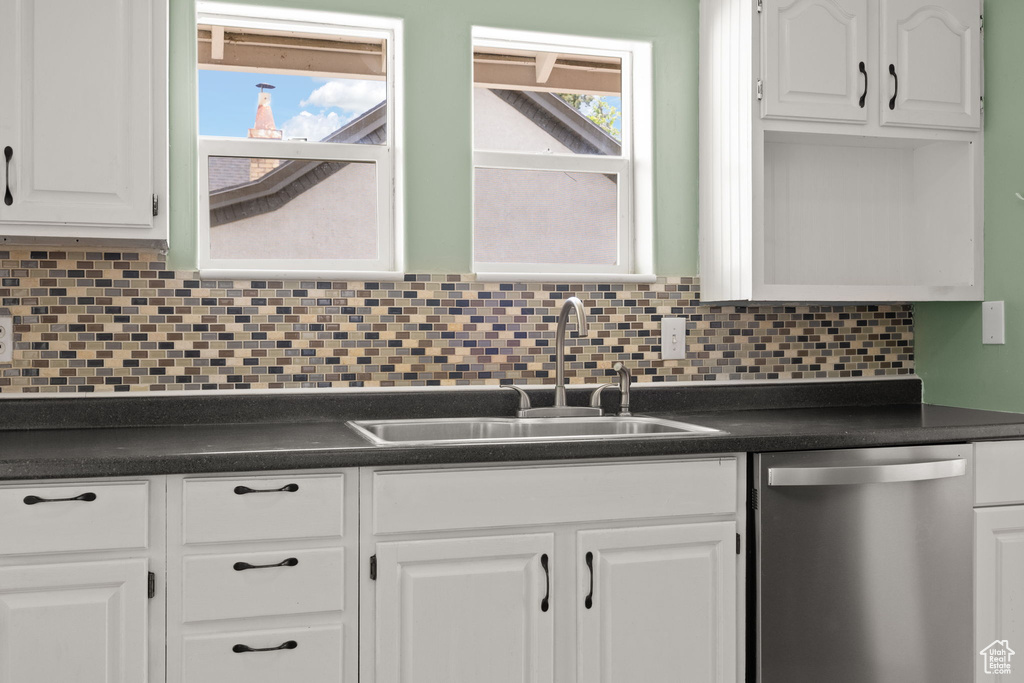 Kitchen featuring stainless steel dishwasher, dark countertops, white cabinets, a sink, and tasteful backsplash