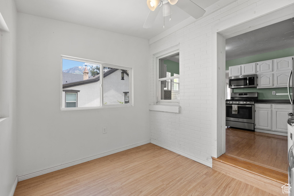 Unfurnished room with light wood-type flooring, a ceiling fan, baseboards, and brick wall