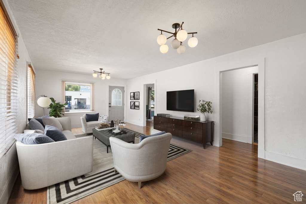 Living area with a chandelier, wood finished floors, a textured ceiling, and baseboards