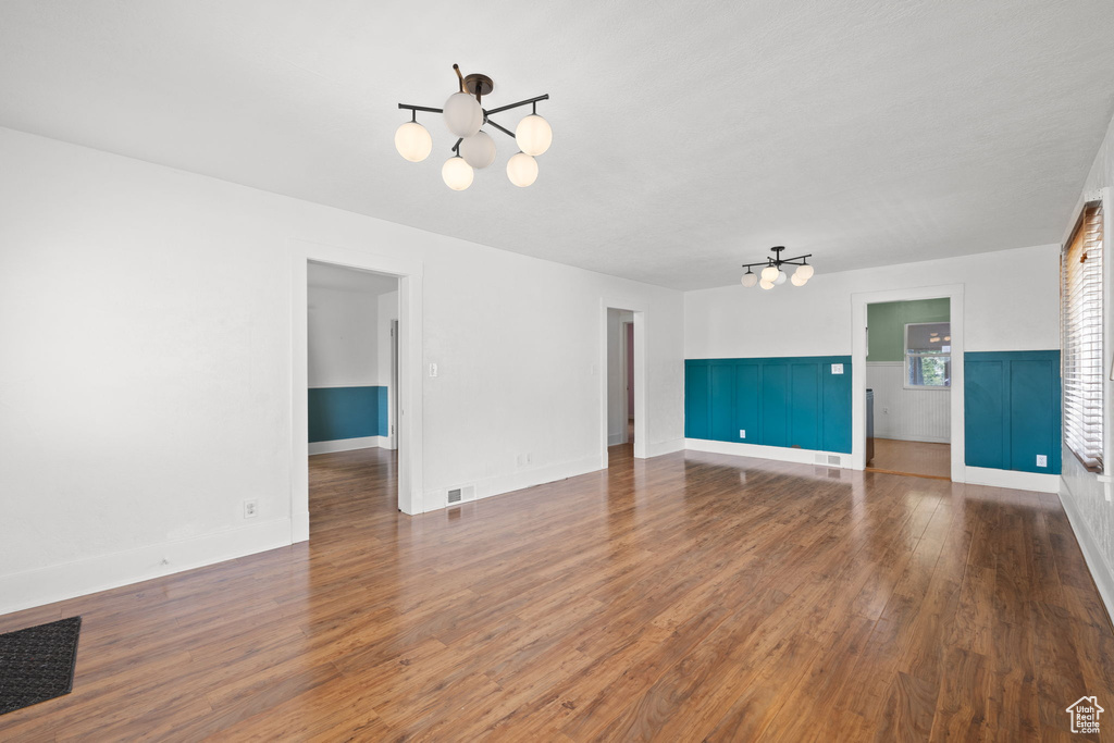 Unfurnished living room with a chandelier, wood finished floors, and a wainscoted wall