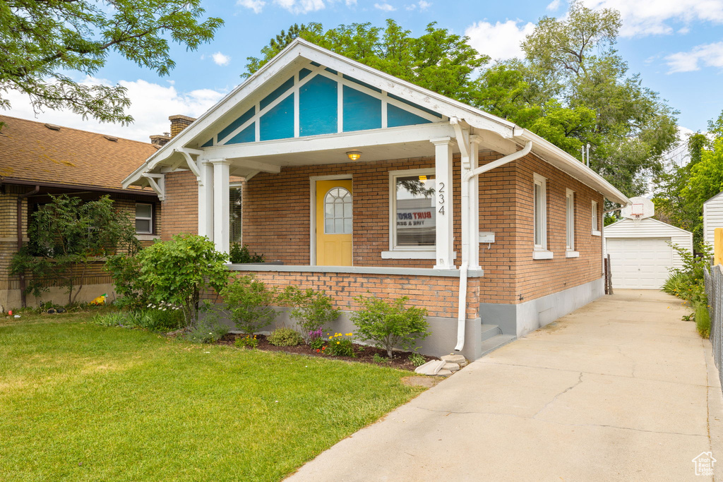 View of front of house featuring an outdoor structure, brick siding, a front yard, and a detached garage