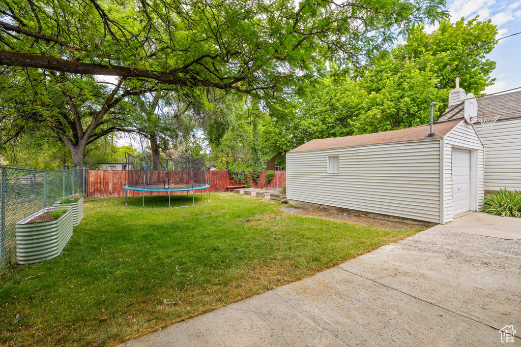 View of yard with a trampoline, an outdoor structure, a garage, and concrete driveway