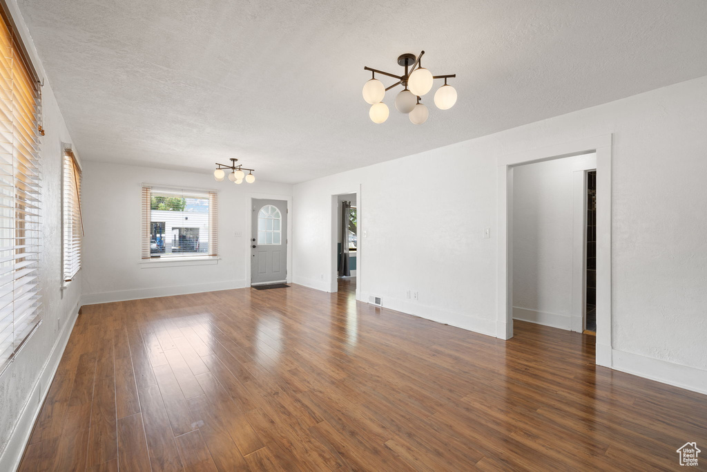 Unfurnished living room featuring a chandelier, dark wood-style flooring, a textured ceiling, and baseboards