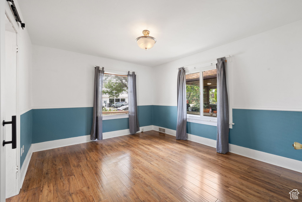 Empty room with a barn door, wood finished floors, and baseboards