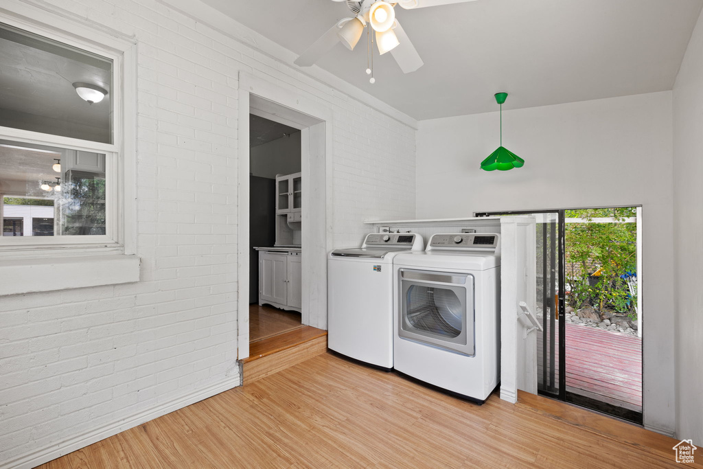 Washroom featuring washing machine and clothes dryer, brick wall, a ceiling fan, and light wood finished floors