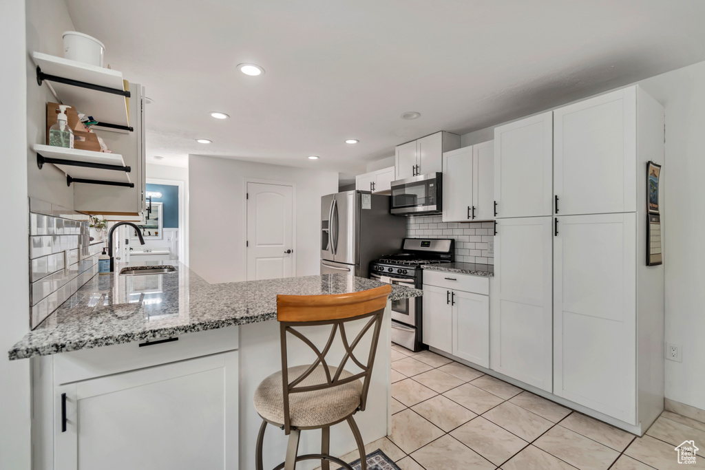 Kitchen featuring stainless steel appliances, a sink, a peninsula, decorative backsplash, and white cabinets