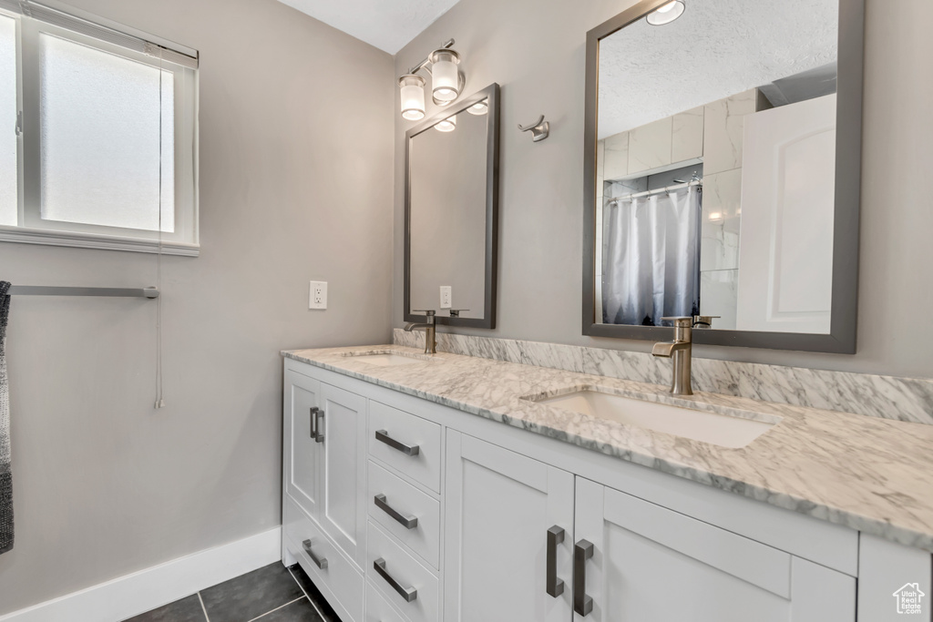 Full bath with double vanity, tile patterned floors, curtained shower, and baseboards