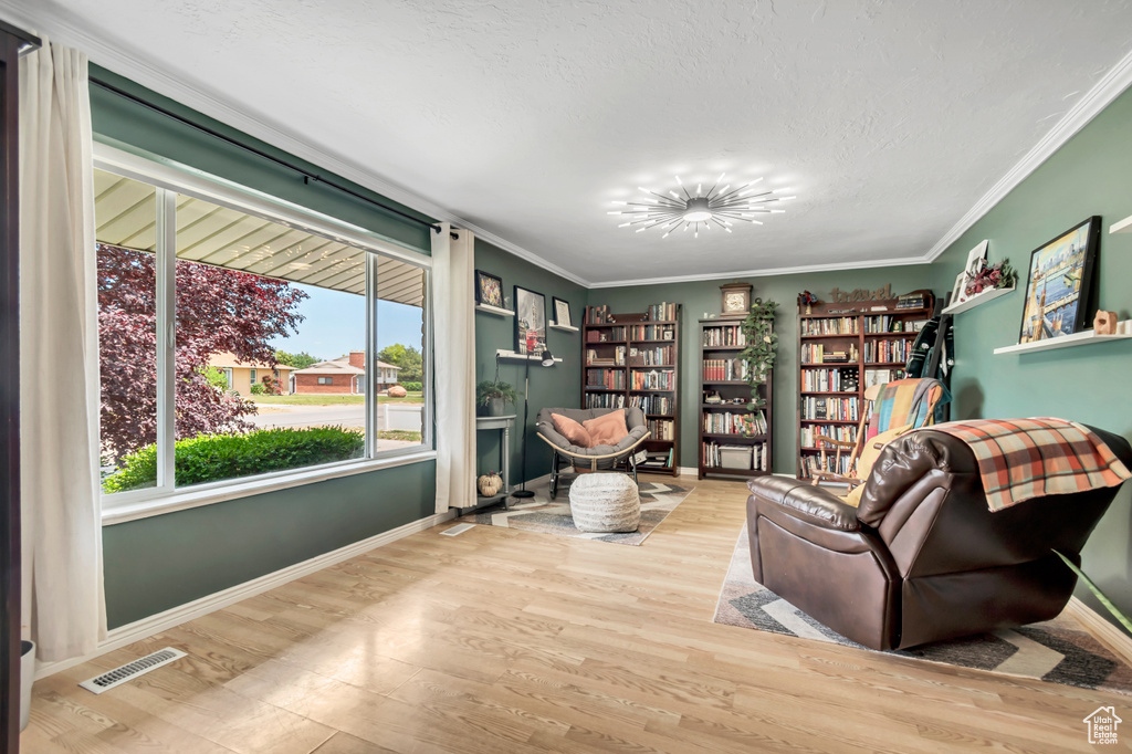 Sitting room with wood finished floors, ornamental molding, baseboards, and a textured ceiling