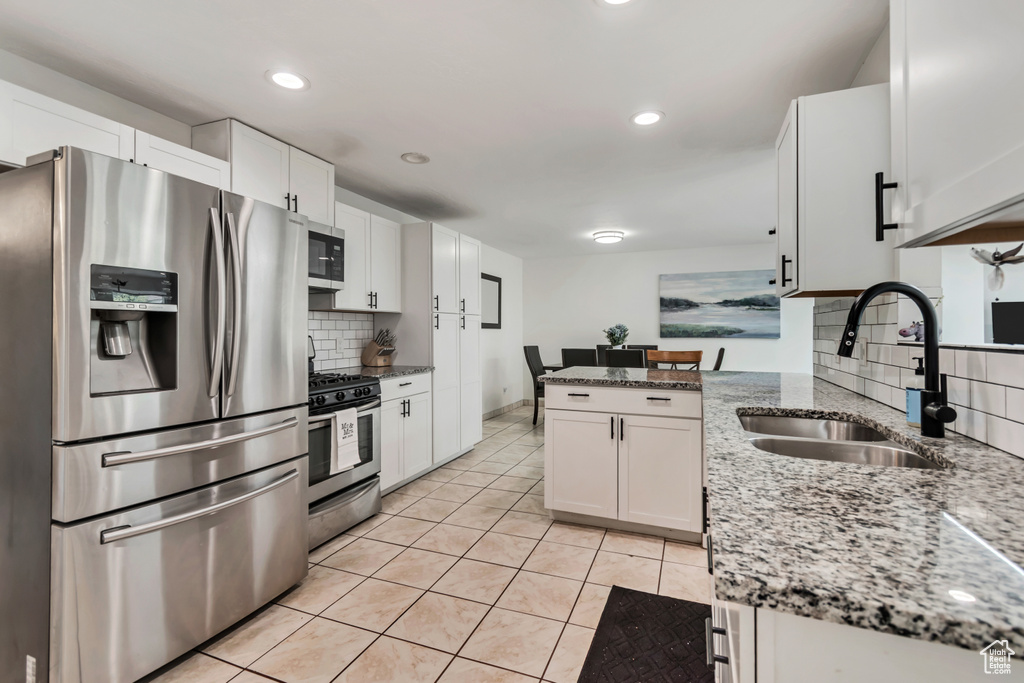 Kitchen featuring stainless steel appliances, a sink, backsplash, light tile patterned floors, and white cabinets