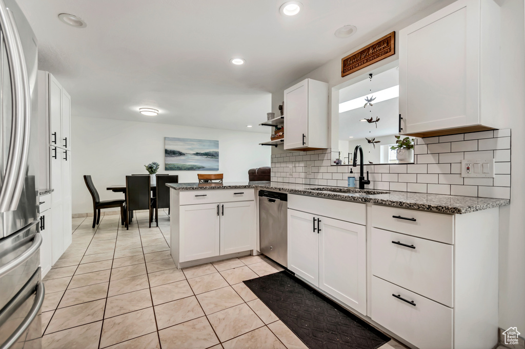 Kitchen with a sink, appliances with stainless steel finishes, white cabinetry, backsplash, and light tile patterned floors