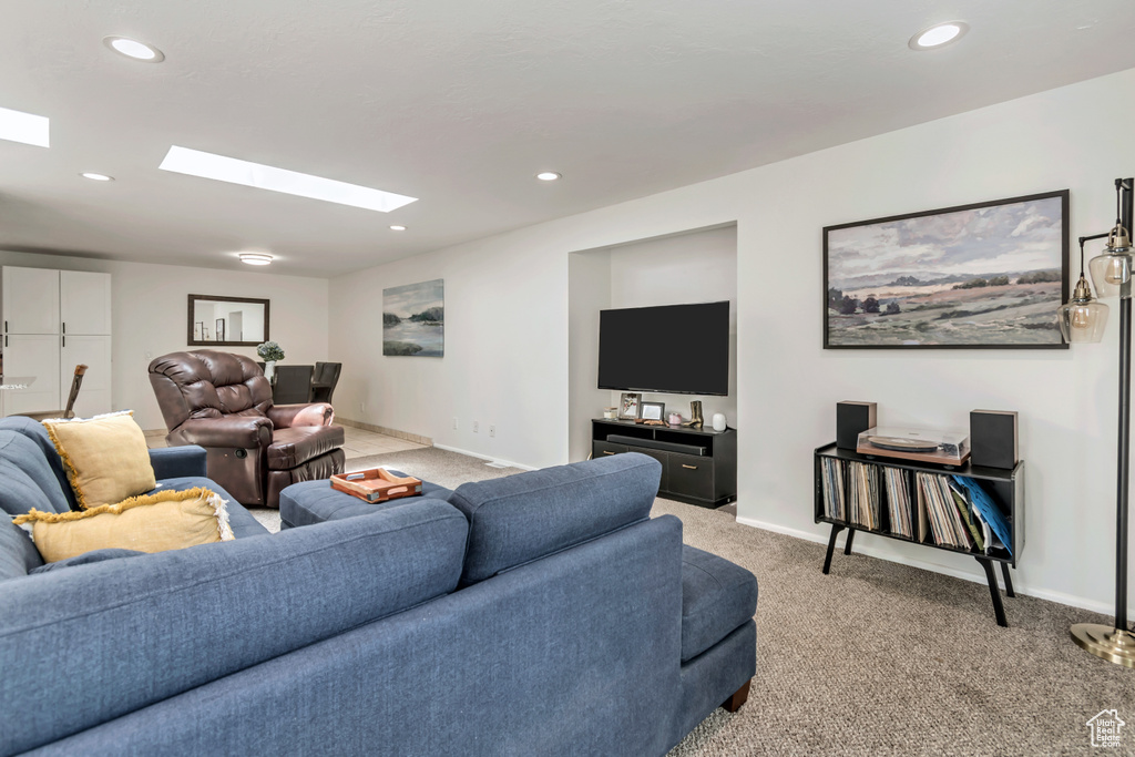 Living area featuring a skylight, light colored carpet, baseboards, and recessed lighting