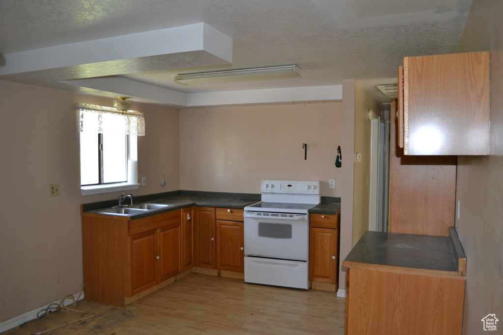 Kitchen featuring white electric stove, light wood-type flooring, a sink, dark countertops, and brown cabinetry