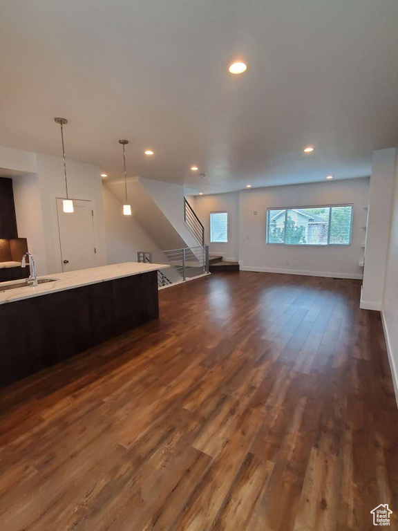 Unfurnished living room with a sink, stairway, dark wood-style flooring, recessed lighting, and baseboards