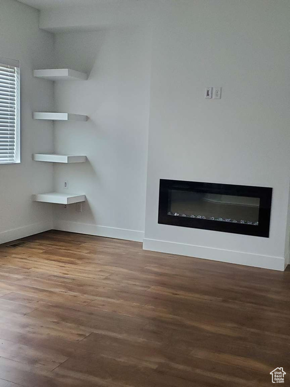 Unfurnished living room featuring a glass covered fireplace, wood finished floors, and baseboards