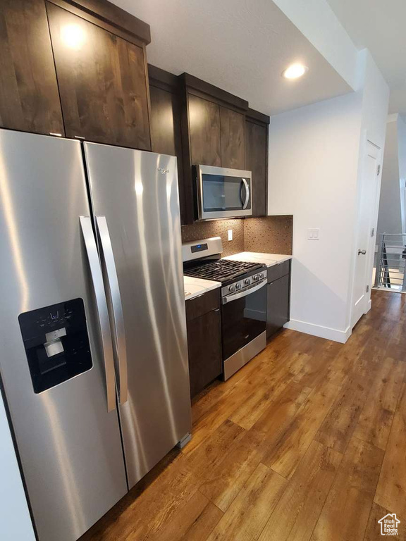 Kitchen with stainless steel appliances, light countertops, dark brown cabinets, wood finished floors, and recessed lighting