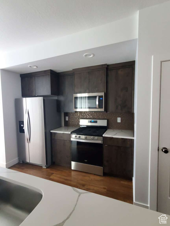 Kitchen with appliances with stainless steel finishes, light countertops, tasteful backsplash, dark brown cabinetry, and dark wood finished floors